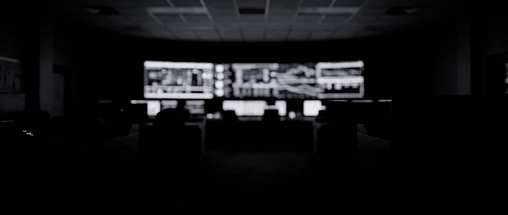 An out-of-focus grid control room at night, a wall of dark monitors glowing faintly